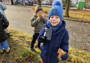 Dzieci przez lornetki i lupy oglądają korę drzewa i liście.