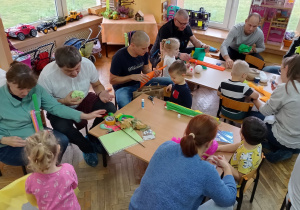 Dzieci robią z rodzicami kukiełki przy stolikach.