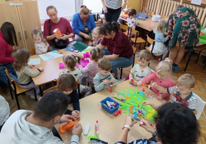 Dzieci robią z rodzicami kukiełki przy stolikach.