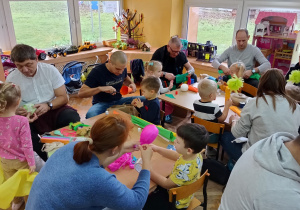 Dzieci robią z rodzicami kukiełki przy stolikach.