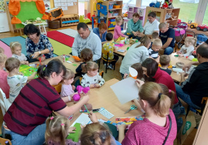 Dzieci robią z rodzicami kukiełki przy stolikach.