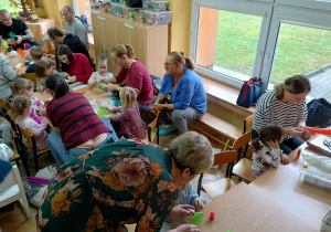 Dzieci robią z rodzicami kukiełki przy stolikach.