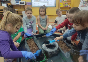 Dziewczynki i chłopcy wsypują torf do doniczek.