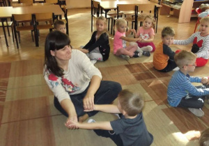 Dzieci siedzą w parach na dywanie i bawią się przy muzyce w taniec rąk.
