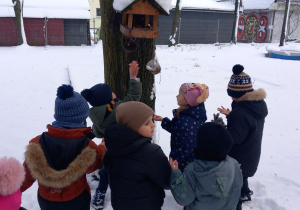 Krasnoludki wsypują pokarm dla ptaków do karmnika.