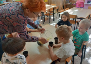 Pani Agnieszka nalewa dzieciom do kubeczków mus z zebranych wcześniej jabłek.