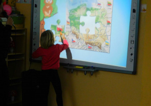 Basia z grupy Słoneczek uklada z puzzli mapę Polski na tablicy interaktywnej.