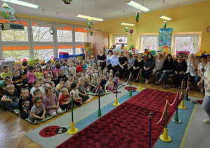 Przedszkolaki i personel siedzą i czekają na pokaz mody.