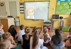 Dzieci z grupy "Biedronek" oglądają film edukacyjny pokazujący, że miasta są najbardziej narażone na zmiany klimatyczne