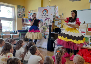 Przedszkolaki siedzą na dywanie, słuchają opowiadania oraz oglądają ilustracje.