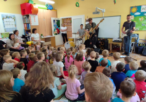 Panowie grają na perkusji oraz na gitarze basowej gitarze elektrycznej.