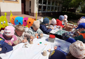 Krasnoludki malują wzory na tekturowych doniczkach.