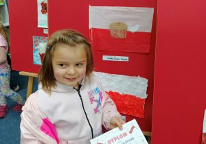 Latika stoi przy tablicy na której wisi jej praca konkursowa.