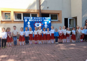 Dzieci z grupy Słoneczek stoją w półkolu i deklamują wiersz „Mama i Tata”.