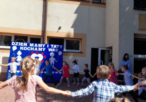 Przedszkolaki tańczą, trzymając się za ręce i tworząc duże koło.