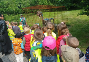 Dzieci oglądają dinozaura zamkniętego w klatce.