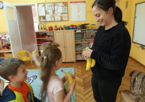 Pani Martyna częstuje przedszkolaki bananami.