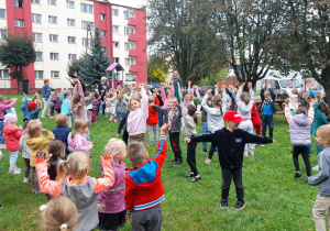 Przedszkolaki przy dźwiękach muzyki wykonują ćwiczenia gimnastyczne.