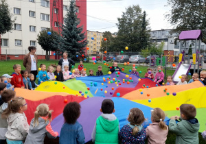 Dzieci trzymając chustę animacyjną, zrzucają jak największą ilość piłeczek.