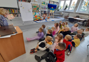 Dzieci siedzą na dywanie i słuchają z zainteresowaniem bajki o myszce.