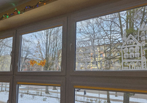 Świąteczne dekoracje okienne z motywem domków, bombek, śnieżynek i choinki.