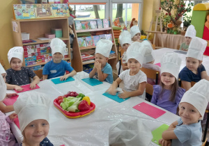 Krasnoludki siedzą przy stole w czapkach kucharskich.