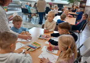 Przedszkolaki siedzą przy stolikach i kolorują liście.