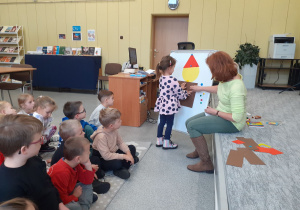 Pani Ilona pomaga Idze przyczepić na tablicy figurę do pajacyka.