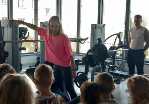 Pani Marta prezentuje dzieciom sprzęt na siłowni.