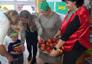 Pani Dyrektor częstuje dzieci pięknym czerwonym jabłuszkiem.