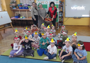Wspólne zdjęcie dzieci z grupy Słoneczek z Panią Dyrektor i nauczycielkami trzymającymi miskę pełną jabłek.