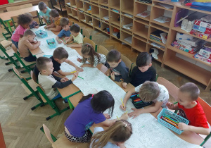 Dziewczynki i chłopcy kolorują malowankę.