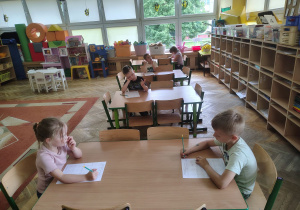 Dzieci siedzą przy stolikach i rozwiązują karty pracy.