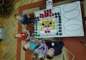 Dzieci siedzą przy ułożonym obrazku z kubeczków na macie do kodowania.