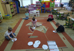 Dzieci ustawiają godzinę na papaierowych zegarach.