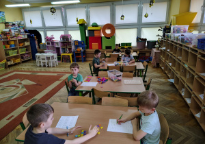 Dzieci rozwiązują przy stolikach karty pracy.